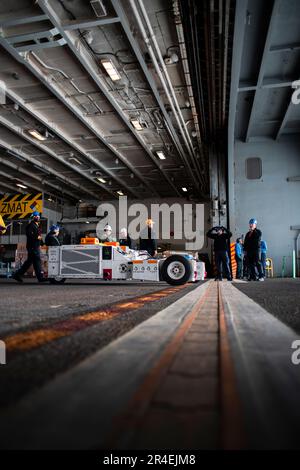 Matrosen, die an Bord des Flugzeugträgers USS George Washington (CVN 73) der Nimitz-Klasse der Flugabteilung zugeteilt sind, bereiten sich auf den Transport eines F/A-18C Hornet vor, das Trainingsflugzeug in die Hangarbucht an Bord der USS George Washington der Nimitz-Klasse (CVN 73) in Newport News, Virginia, 28. März 2023. George Washington wird im Newport News Shipbuilding den Tankkomplex überholen (RCOH). RCOH ist ein mehrjähriges Projekt, das nur einmal während der 50-jährigen Lebensdauer eines Frachtführers durchgeführt wird und das Betanken der beiden Kernreaktoren des Schiffs sowie umfangreiche Reparaturen, Aufrüstungen und Modernisierungen umfasst. (USA Navy Foto B Stockfoto