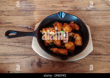 Blick von oben auf koreanisches gebratenes Hähnchen auf schwarzem Eisenteller und Holztisch. Stockfoto