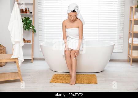 Wunderschöne junge asiatische Frau, die Körpercreme auf das Bein im Badezimmer aufträgt Stockfoto