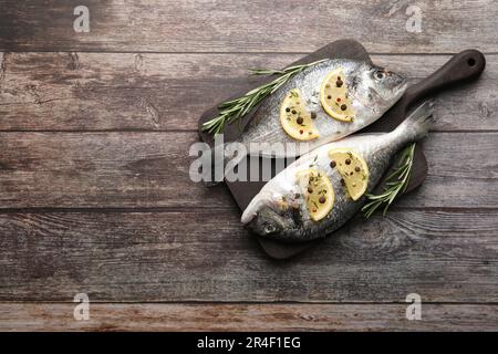 Frischer dorado-Fisch, Zitronenscheiben und Rosmarin-Zweige auf Holztisch, Draufsicht. Platz für Text Stockfoto