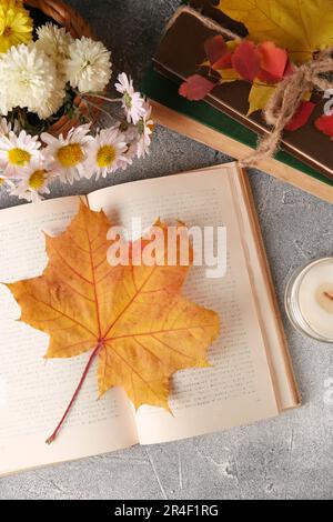 Bücher mit Herbstblättern als Lesezeichen, Duftkerze und wunderschönen Blumen auf einem hellgrauen strukturierten Tisch, flach liegend Stockfoto