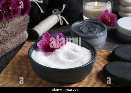 Wunderschöne Zusammensetzung mit Meersalz, brennenden Kerzen, Blumen und verschiedenen Spa-Produkten auf grauem Tisch Stockfoto