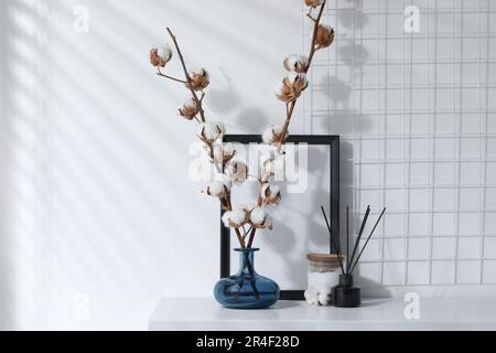 Reed-Diffusor, Kerze und Baumwollzweige mit flauschigen Blumen auf weißem Holztisch im Innenbereich Stockfoto