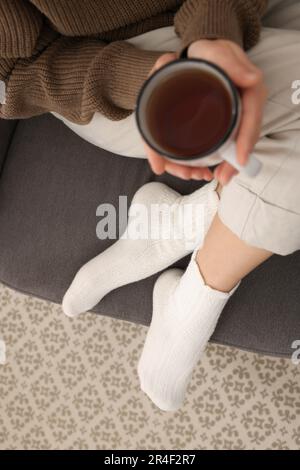 Eine Frau in warmen Socken, die sich zu Hause mit einer Tasse Tee entspannt, über der Aussicht Stockfoto