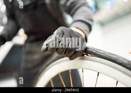 Nicht erkennbarer Fahrradmechaniker mit Schutzhandschuhen, der einen luftlosen Reifen in einer Reparaturwerkstatt von einem Rad entfernt. Selektive Fokuszusammensetzung mit Stockfoto