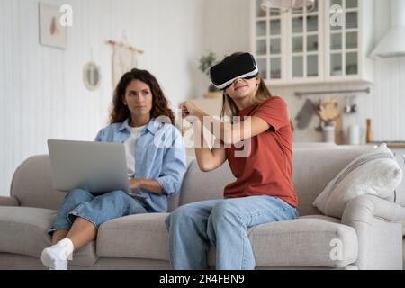 Von der Mutter zu Hause aus, die sich die aufgeregte kleine Tochter im VR-Helm anschaut, die Spiele spielt Stockfoto