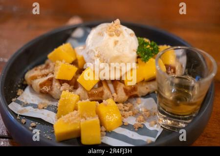 Croffle, eine Mischung aus Croissant und Waffel mit Mango, Eis und Honig, serviert auf einem Teller Stockfoto
