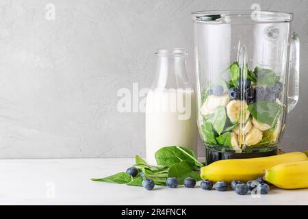 Zutaten für Heidelbeeren, Bananen und Spinat in Mixer und Milchflasche zum Kochen von Heidelbeeren und Bananen-Milchshake Stockfoto