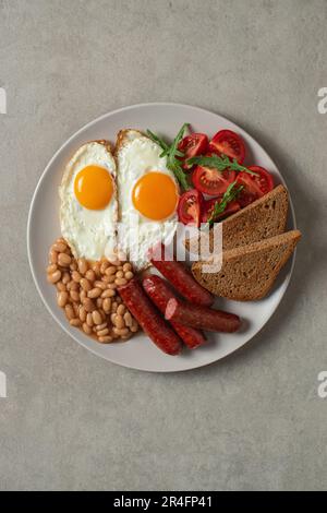 Spiegeleier mit Würstchen und Bohnen auf einem Teller mit grauem Hintergrund. Englisches Frühstück Stockfoto