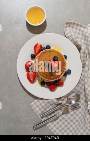 Pfannkuchen mit Beeren und Honig auf einem grauen Tisch Stockfoto
