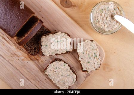 Dunkles Brot auf Holzbrett mit Aufstrich und Frühlingszwiebeln Stockfoto