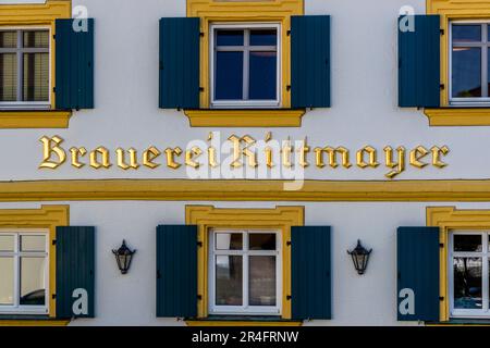 Die Schrift „Brauerei Rittmayer“ leuchtet in Gold auf der weiß-gelben Fassade des Gasthauses in Willersdorf, Bayern, Deutschland, zwischen türkisfarbenen Fensterläden. Stockfoto