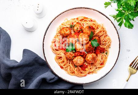 Gekochte Spaghetti-Pasta mit Fleischbällchen und scharfer Tomatensoße mit Petersilie auf dem Teller, weißer Tischhintergrund, Draufsicht Stockfoto
