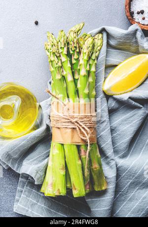 Frischer Spargel, Salz, Pfeffer, Zitrone und Olivenöl auf grauem Stein Küchentisch Hintergrund, Draufsicht, Kopierbereich Stockfoto