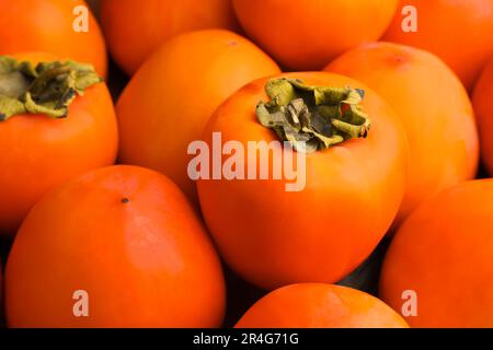 Ein Haufen köstlicher reifer, saftiger Persimonen als Hintergrund, Nahaufnahme Stockfoto