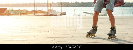 Junger Mann, der Rollschuhlaufen auf dem Pier in der Nähe des Flusses macht, Platz für Text. Bannerdesign Stockfoto