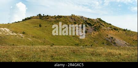 Wunderschöne Aussicht von unten auf den Hügel und die Wolken an einem sonnigen Sommertag. Gras, Bäume und viele Steine wachsen auf Hügeln. Kleine Steine gießen in nicht-wea herunter Stockfoto