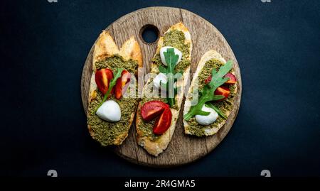 Bruschettas mit Pesto, Tomaten, Mozzarella-Käse und Basilikum auf Holzbrett. Italienisches Toastbrot mit Gemüse und traditioneller Sauce Stockfoto