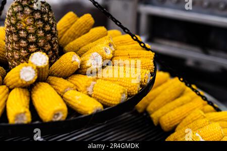 Gekochter Mais und Ananas bei Straßenmarkt-Schließung. Frisches gelbes Gemüse, Mais und Obst auf einem traditionellen Festival Stockfoto