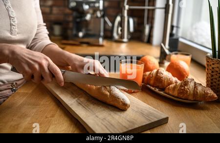 Ein Mädchen hat französisches Baguette mit Messer in der Küche geschnitten. Leckeres rustikales frisches Brot aus Frankreich zum Frühstück Stockfoto