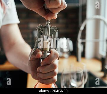 Ein Mann öffnet eine Flasche Wein und Gläser auf dem Tisch in der Küche Stockfoto