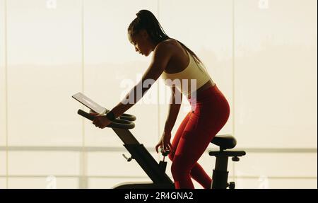 Schwarze Frau, die sich auf ihrer Fitness-Reise auf neue Höhen stürzt und an einem herausfordernden virtuellen Radkurs teilnimmt. Eine Frau, die ihre Fitness zerstört Stockfoto