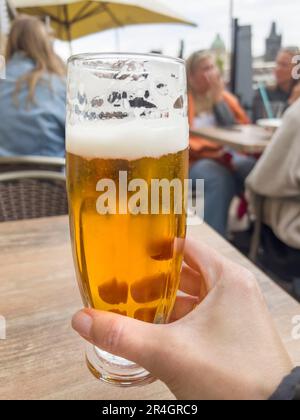 Bier, weibliche Hand hält ein Glas kaltes Bier mit selektivem Fokus auf verschwommene Menschen in einem Café oder Restaurant. Konzeptfoto Alkohol Stockfoto