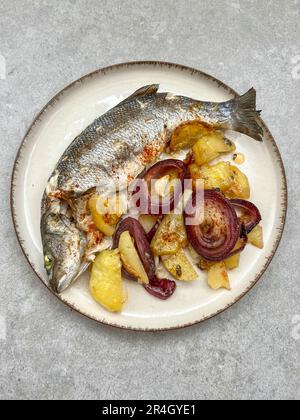 Meeresfrüchte, Blick von oben köstliche gegrillte Seebarschfische auf Teller, serviert mit Kartoffeln und Zwiebeln auf grauem Hintergrund oder Oberfläche mit selektivem Fokus. Heidenmeer Stockfoto