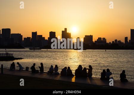 Blick von Odaiba, Tokio, über die Bucht bis zur Skyline von Tokio bei Sonnenuntergang mit Silhouetten von unbekannten Menschen im Vordergrund Stockfoto