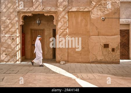 Ein arabischer Mann in weiß geht neben einem alten Haus in einer Straße in Al Fahidi, einem historischen Viertel in Dubai, Vereinigte Arabische Emirate Stockfoto