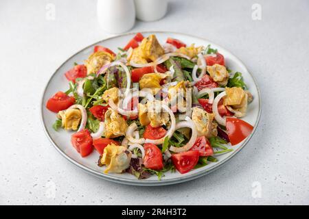 Warmer Salat mit rapan (Schnecken), Tomaten, Zwiebeln, Blattgemüse und Olivenöl. Traditioneller Salat mit Meeresfrüchten. Nahaufnahme, selektiver Fokus. Stockfoto