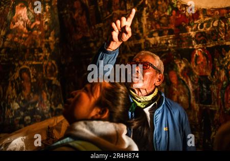 (230528) -- ZANDA, 28. Mai 2023 (Xinhua) -- Rigzin Wangzhab stellt Touristen Wandbilder in einer Grotte in der Präfektur Zanda County der Präfektur Ngari, Südwestchina, Autonome Region Tibet, vor, 26. Mai 2023. Versteckt zwischen Sandsteinhügeln im abgelegenen Westen Tibets liegt ein Abschnitt von honigwabenförmigen Höhlen weit außerhalb der Reichweite der meisten Reisenden. Die 1.000 Jahre alten Höhlen in der Präfektur Ngari in der Autonomen Region Tibet, die als Donggar- und Piyang-Grotten bekannt sind, beherbergen eine der weltweit größten Sammlungen tibetischer buddhistischer Wandbilder. Rigzin Wangzhab, 75, bewacht das Gelände seit über 20 Jahren. Stockfoto