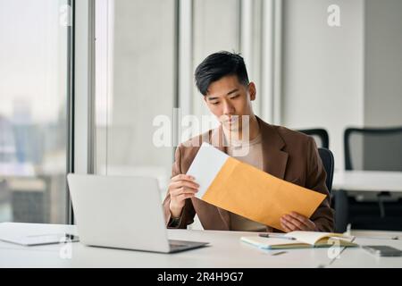 Ein junger asiatischer Geschäftsmann, der im Büro einen Geschäftsbrief erhält. Stockfoto