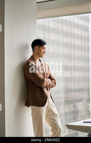 Ein junger, selbstbewusster Geschäftsmann aus Asien, der auf Fensterdenken schaut. Stockfoto