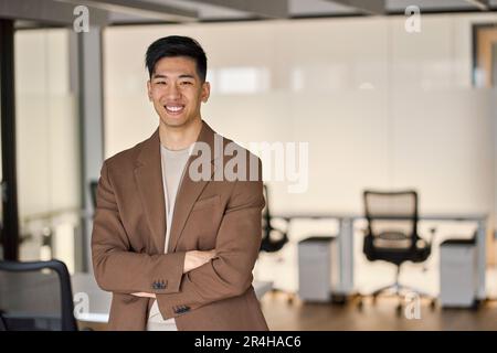 Junger, glücklicher asiatischer Geschäftsmann, der im Büro vor der Kamera steht. Porträt. Stockfoto