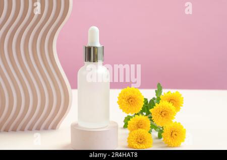 Ätherisches Öl oder Serum und gelbe Chrysanthemen auf einem beigen Podium Stockfoto