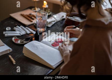 Künstlerin sitzt am Tisch mit brennenden Kerzen in einem Skizzenbuch Stockfoto