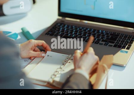 Nahaufnahme einer modernen Frau mit Laptop schreibt in einem Notizbuch. Stockfoto
