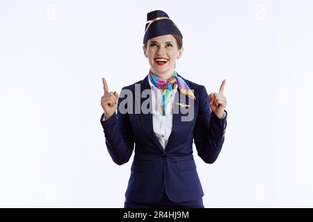 Lächelnde, moderne weibliche Stewardess vor weißem Hintergrund in Uniform, die auf etwas zeigt. Stockfoto