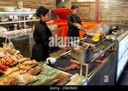 Siem Reap, Kambodscha, Dezember 2018. Zwei Mädchen kochen in schwarzen Kleidern in einem Straßencafé in einer asiatischen Nachtstadt. Asiatische Küche, Street Food. Stockfoto