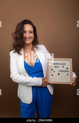 Lächelnde Coacherin, die eine Tafel zeigt. Demokratisches und motivierendes Management. Isoliert auf braunem Hintergrund. Stockfoto