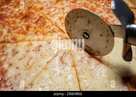 Gebackene und geschnittene Pizza margherita mit einem Pizzaschneider aus nächster Nähe Stockfoto