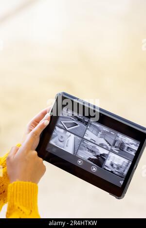 Gekürzte Hände einer birassischen jungen Frau, die ein digitales Tablet hält und ihr Zuhause mit der Kamera kontrolliert Stockfoto