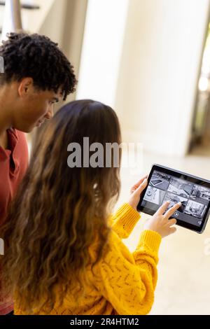 Ein birassistisches junges Paar, das mit einer Videokamera über ein digitales Tablet das Haus kontrolliert Stockfoto