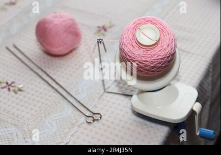 Aufwickeln von rosafarbenem Wollgarn vom Verwickeln bis zum Aufwickeln mit einem Coiler auf dem Tisch Stockfoto