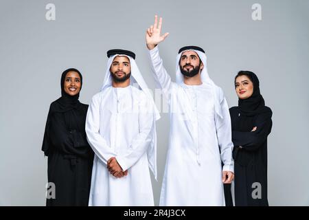 Wunderschöne arabische Frauen aus dem Nahen Osten mit traditionellem Abaya-Kleid und ein Mann aus der Mitte ostern, der Kandora im Studio trägt - Gruppe arabisch-muslimischer Erwachsener Portier Stockfoto