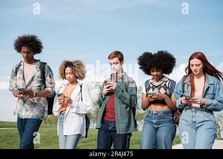 Gruppe von Studenten, die durch den Universitätscampus laufen und nur auf das Mobiltelefon schauen. Konzept: Smartphone, digitales Zeitalter, Unterhaltung Stockfoto