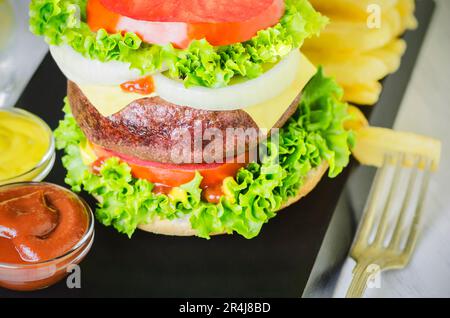 Köstlicher Riesenburger mit gegrilltem Rindfleisch, großer, riesiger klassischer Burger mit Pommes Frites und frischem Gemüse. Stockfoto