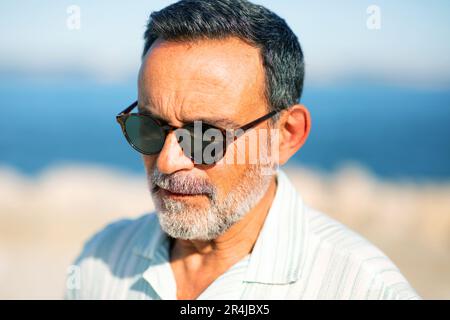 Porträt Eines Alten Mannes, Der Sich In Der Nähe Von See Draußen Posiert Und Eine Sonnenbrille Trägt Stockfoto