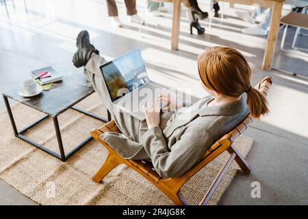 Blick von oben auf eine Geschäftsfrau, die ihren Laptop benutzt, während sie im Bürostuhl sitzt Stockfoto